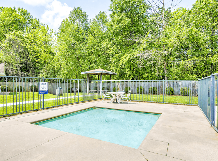 Fenced in hot tub with patio chairs and tree-line in background